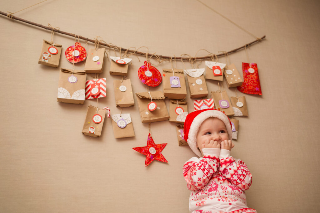 Bébé en bonnet de Père Noël devant un calendrier de l'Avent fait maison en pochettes de papier kraft numérotées