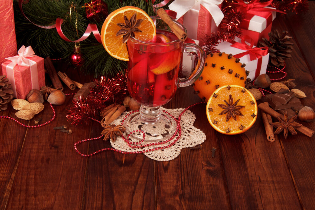 Infusion de Noël aux agrumes et aux épices servie dans un verre, entourée de cannelle, d'anis étoilé et de cadeaux