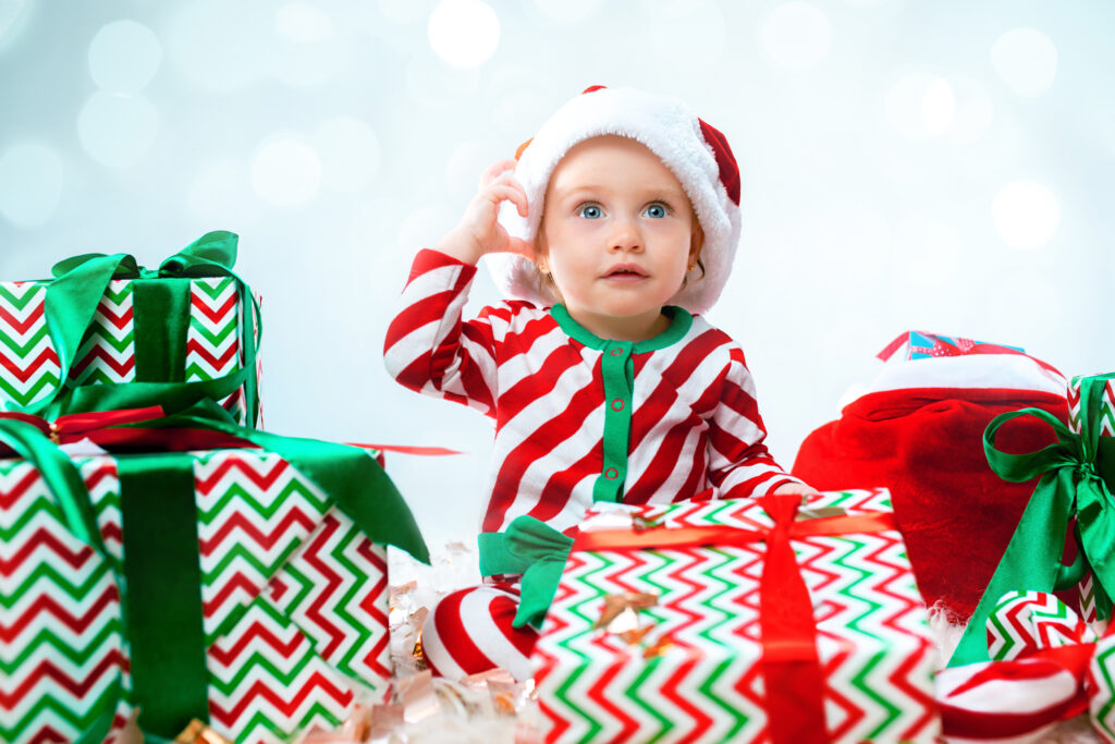 Bébé surpris en tenue de Noël avec cadeaux, idéal pour article sur cadeaux enfants 1-3 ans.