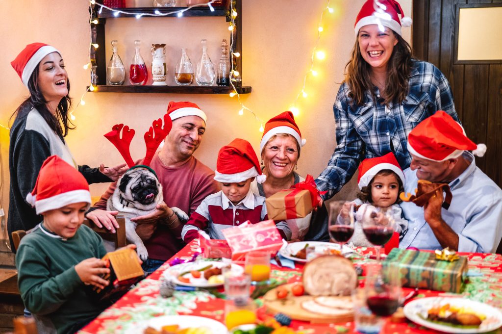 Réunion de famille joyeuse autour d'une table de Noël décorée avec vaisselle de Noël, nappes festives et accessoires, démontrant comment organiser un repas de Noël à la maison pour de nombreux invités.