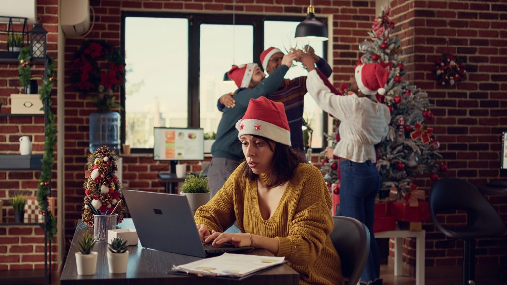 Collègue contrariée devant son ordinateur pendant que les autres décorent le sapin du bureau