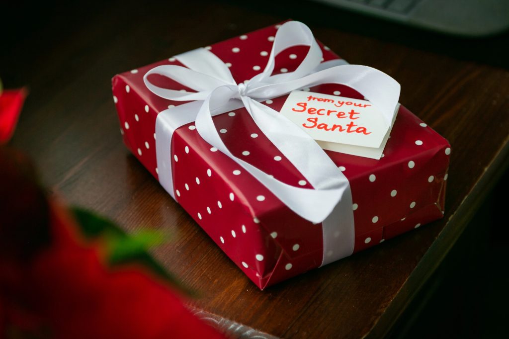 Cadeau rouge à pois blancs avec une étiquette « from your Secret Santa » posé sur une table en bois