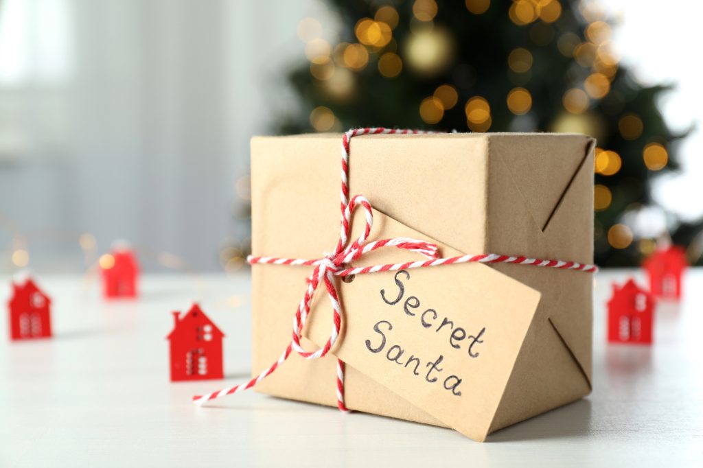 Cadeau en papier kraft ficelé d'un cordon rouge et blanc avec une étiquette Secret Santa, devant un sapin illuminé