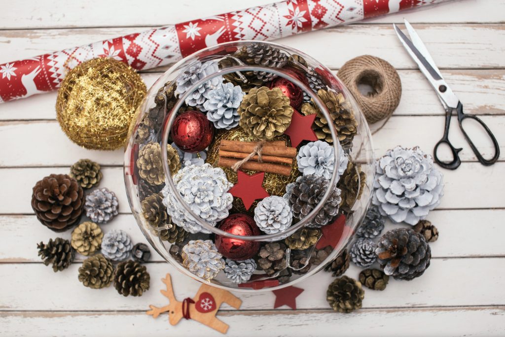 Centre de table DIY : bocal en verre rempli de pommes de pin, de boules rouges et de bâtons de cannelle
