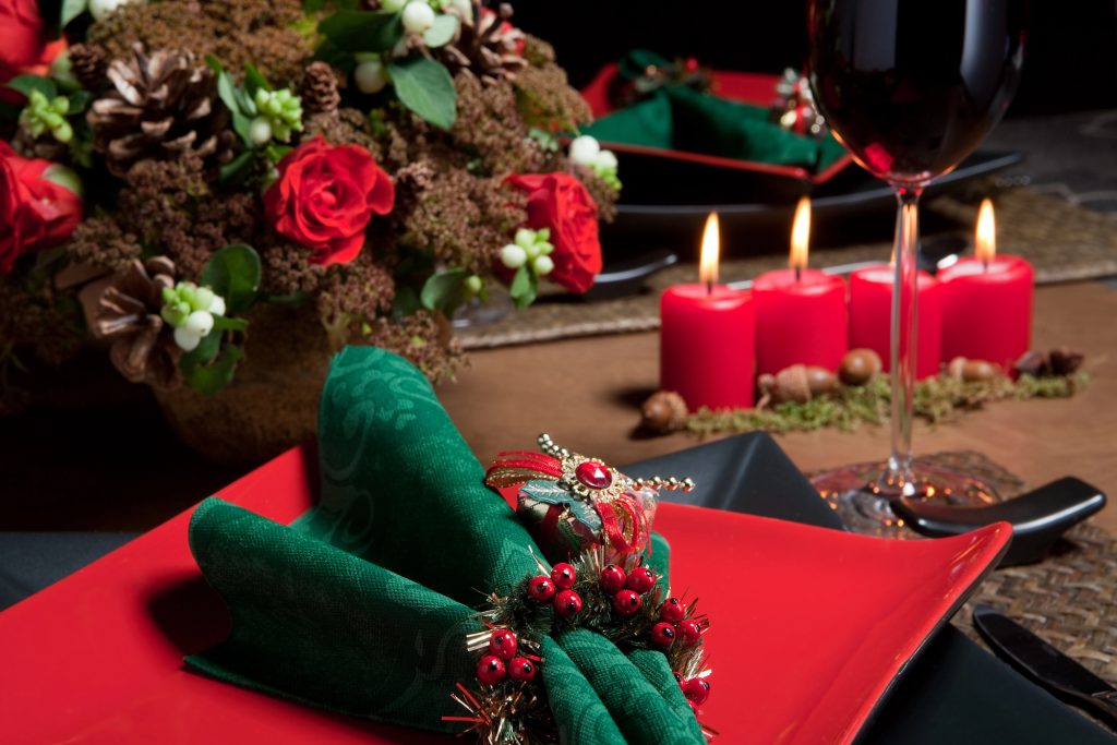 Table de Noël traditionnelle rouge et vert : assiette rouge, serviette verte à rond de houx et bougies allumées