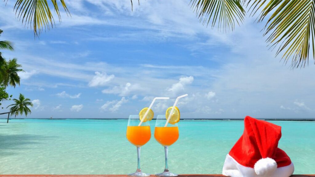 Noël à Tahiti : deux cocktails de fruits et un bonnet de Père Noël posés face au lagon turquoise, sous les palmes
